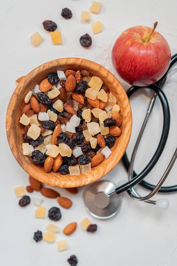 Top view of a healthy mix of nuts and dried fruits with an apple and stethoscope.