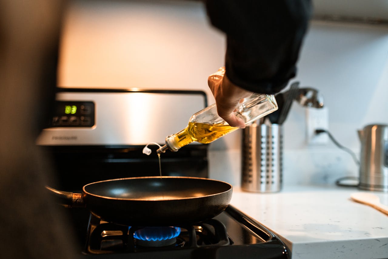 Services Back view crop unrecognizable person pouring olive or sunflower oil into frying pan placed on stove in domestic kitchen