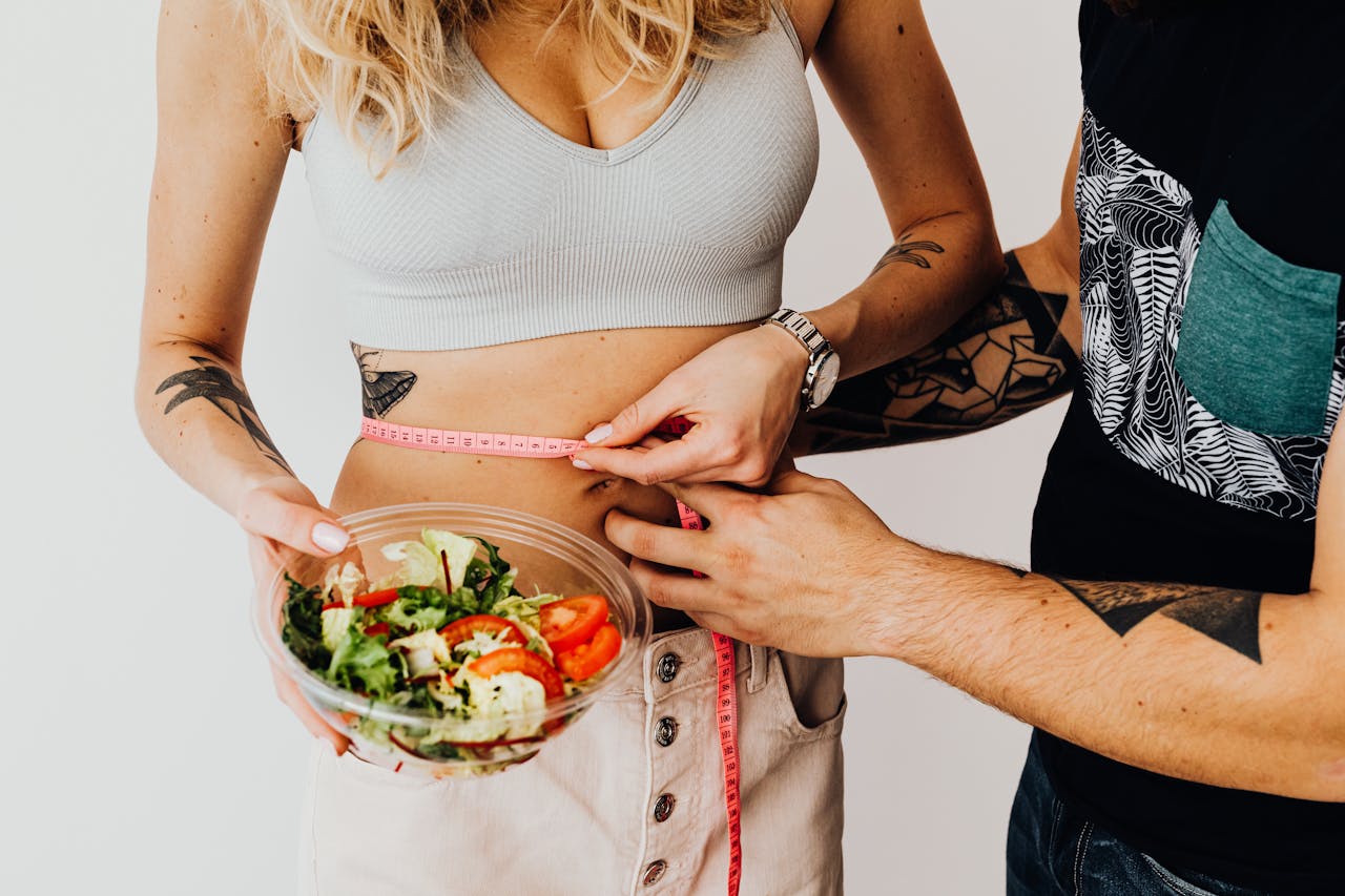 Services A couple measuring waistline with a tape and holding a fresh salad bowl, focusing on fitness and weight loss.