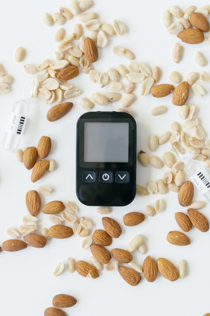 About A top view of a glucose meter surrounded by almonds, syringes, and peanuts on a white background.